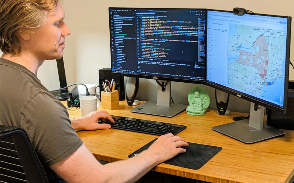 Nick at his desk with screens showing mapping and coding