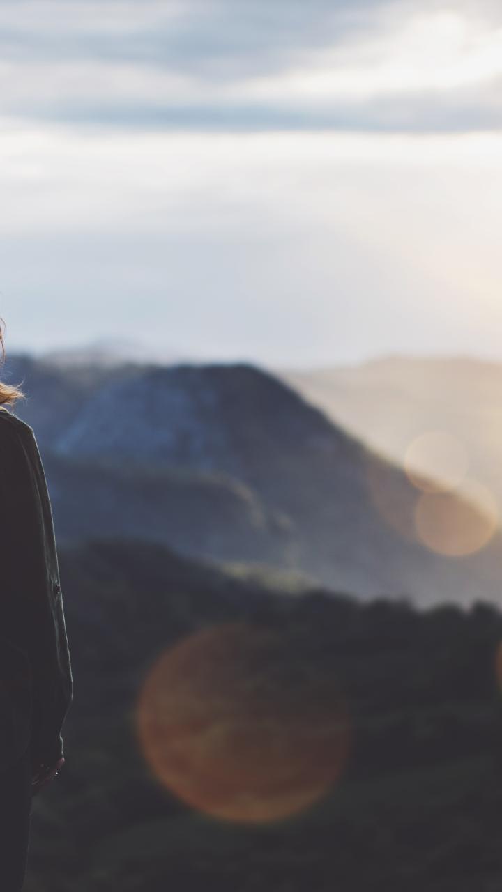 Woman with backpack looking out to a mountainous horizon at sunset