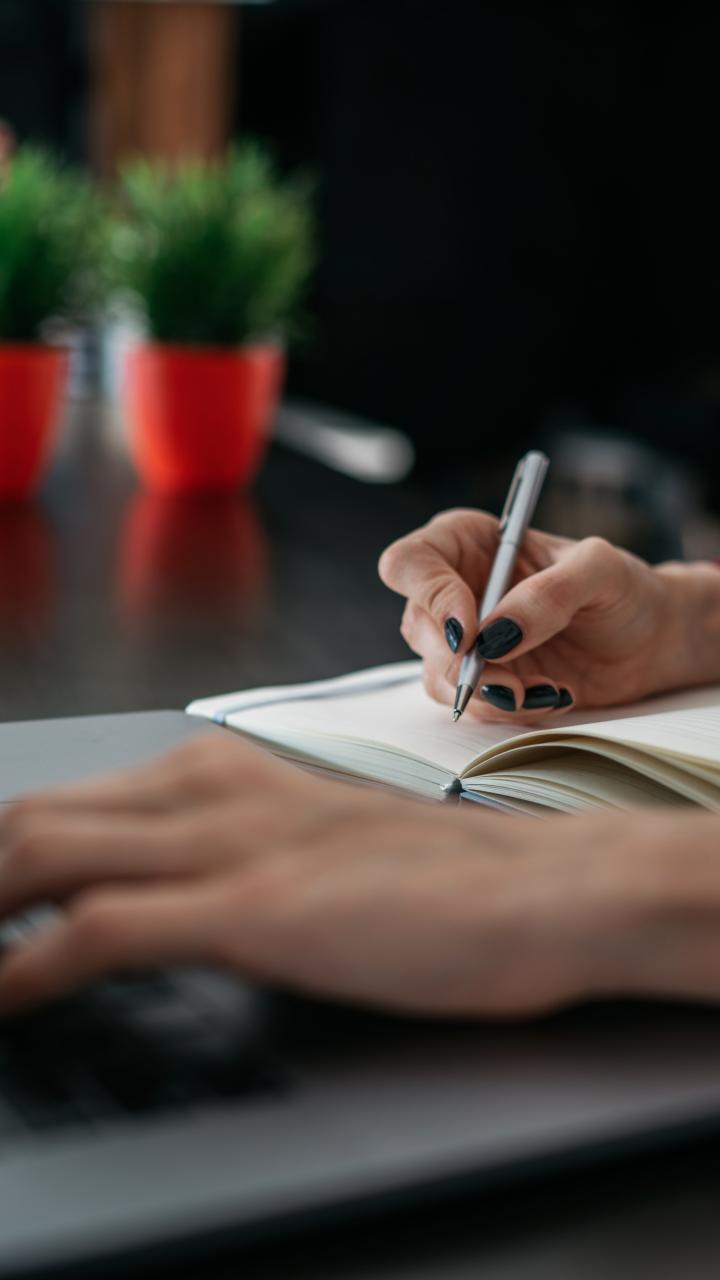 woman typing on laptop and writing in notebook