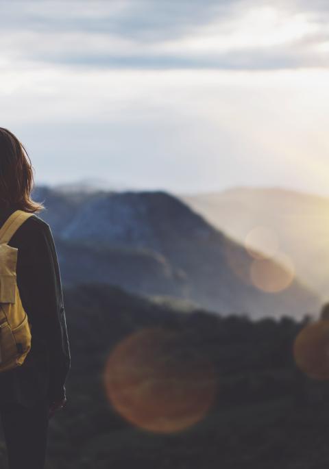 Woman with backpack looking out to a mountainous horizon at sunset