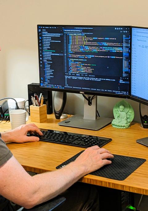 Nick at his desk with screens showing mapping and coding