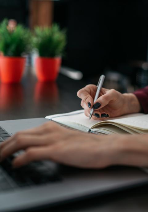 woman typing on laptop and writing in notebook