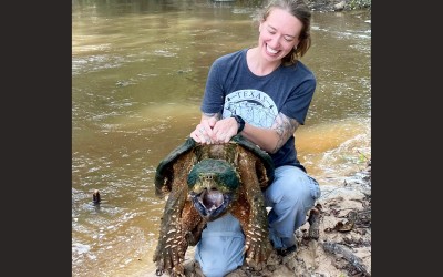 Melissa holding a large alligator snapping turtle on at the water's edge