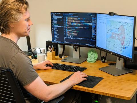 Nick at his desk with screens showing mapping and coding