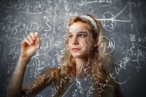 Blonde woman writing math equations on clear board