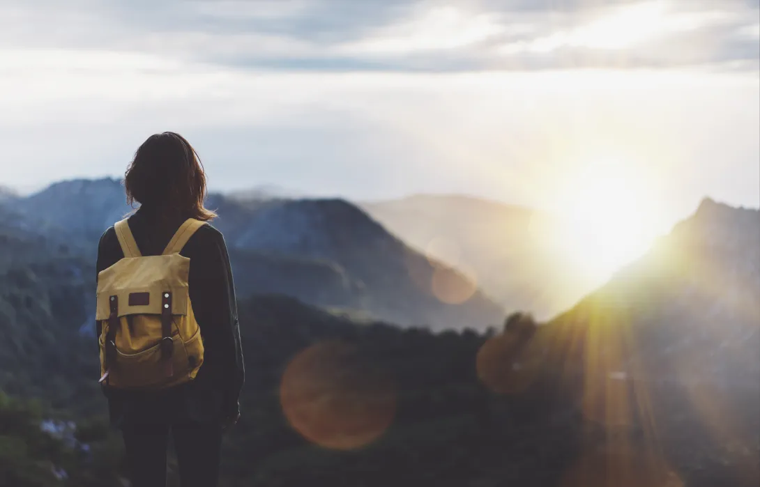 Woman with backpack looking out to a mountainous horizon at sunset