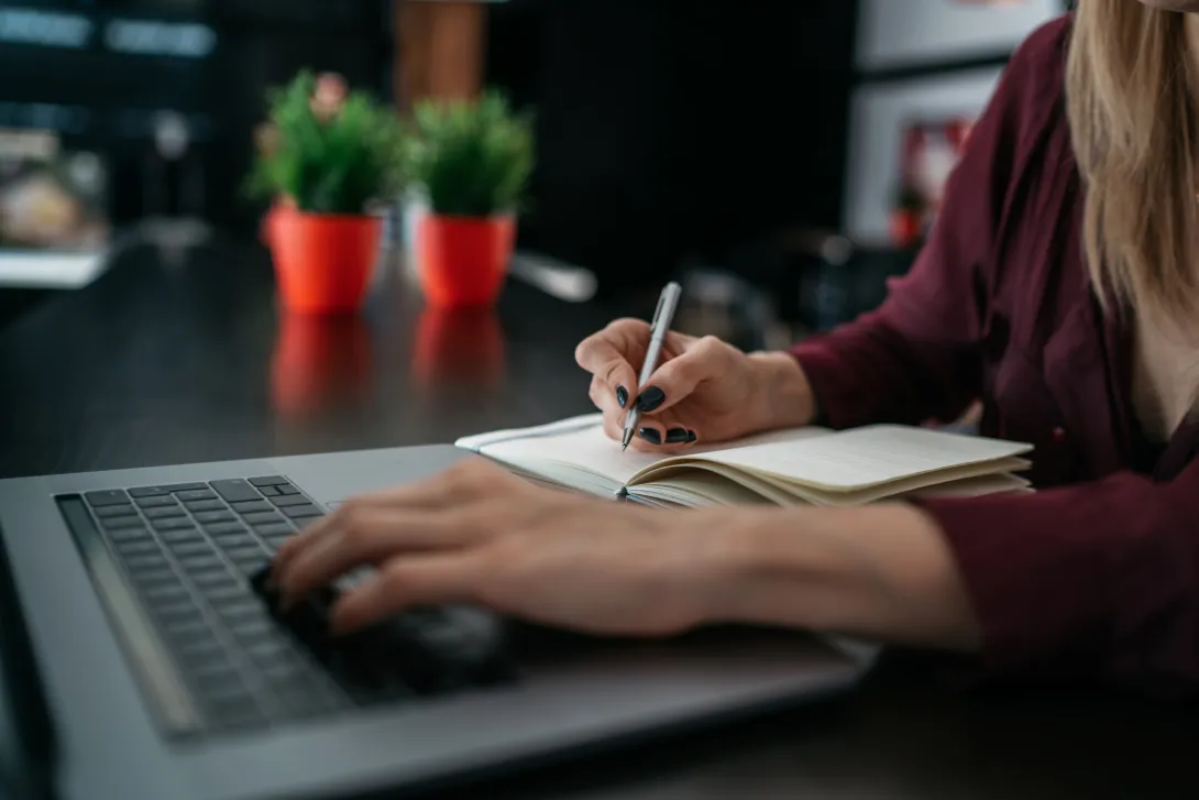 woman typing on laptop and writing in notebook