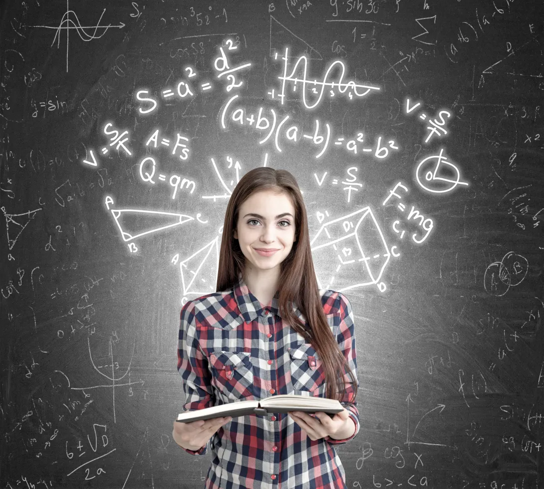 Portrait of a young girl holding an open book while standing near formulas written on a blackboard behind her.