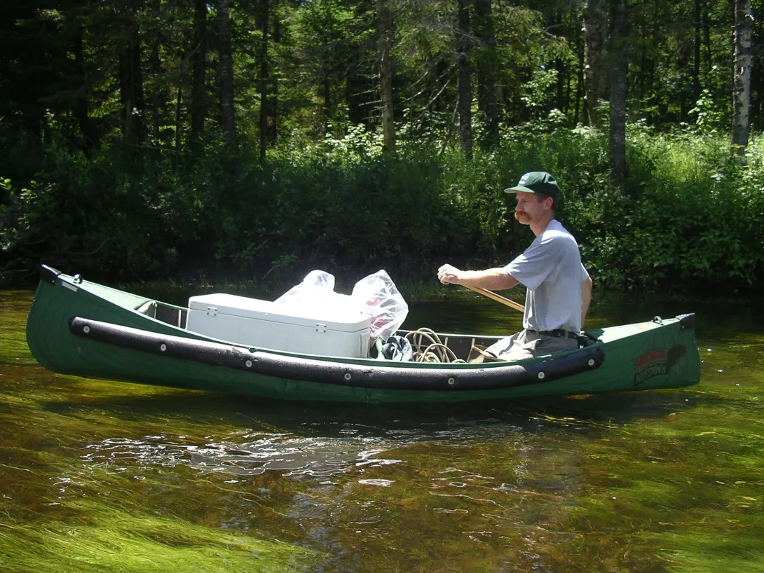 Kevin in a green canoe on water with a white coopler of supplies